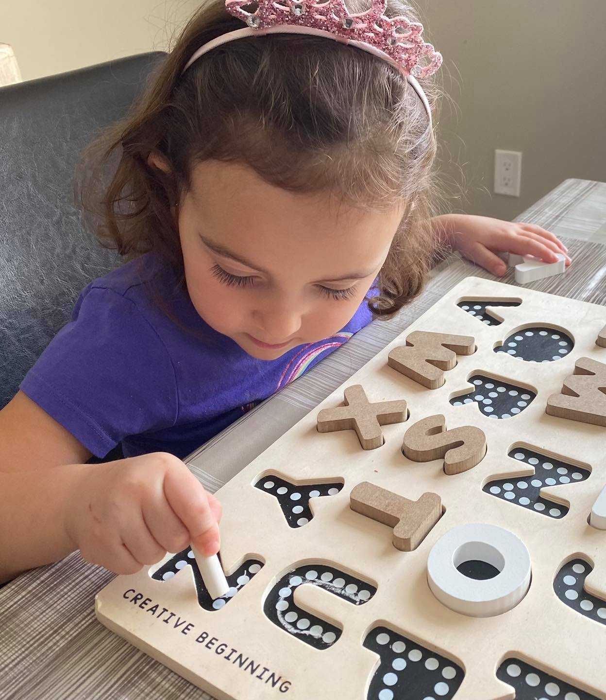 Child playing with alphabetical puzzle on chalkboard base with tracers educational toy